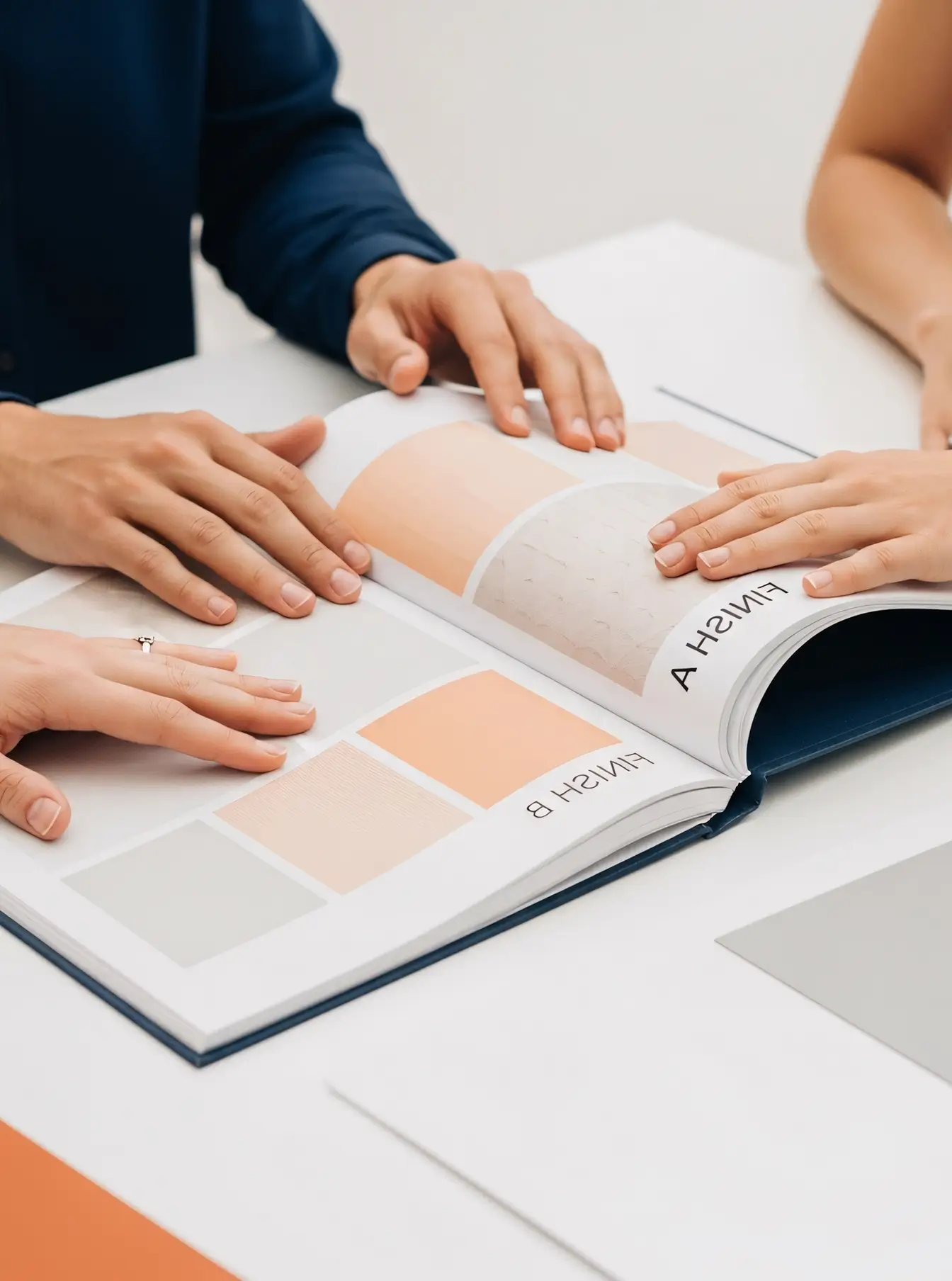 Three people sitting at a table reviewing a sample book displaying color swatches labeled Finish A and Finish B in shades of beige and peach.