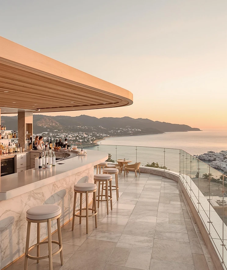 Modern rooftop bar with a marble counter and wooden stools overlooking a coastal town and calm sea at sunset.